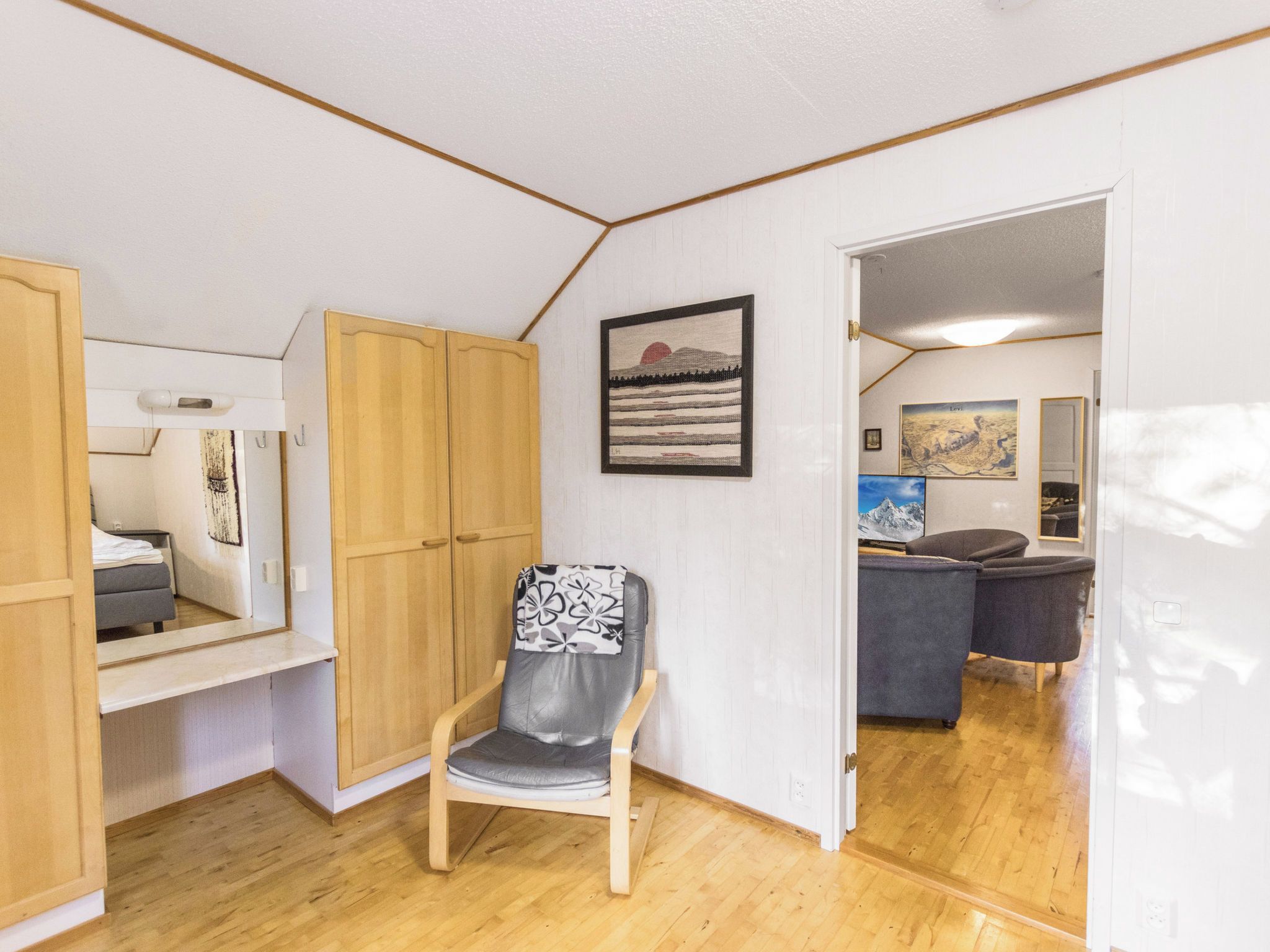 A compact room with a wooden wardrobe, a chair with a patterned cushion, and a bed with a white duvet.