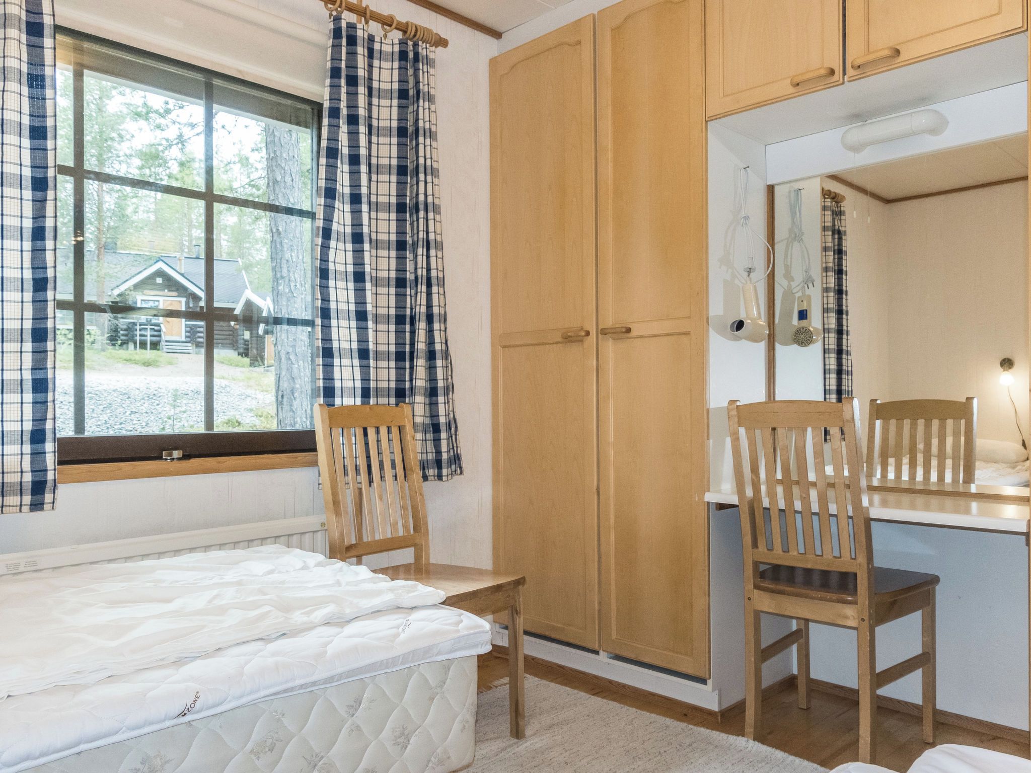 A bedroom with a bed, a wooden wardrobe, a desk with a chair, and a window with curtains.