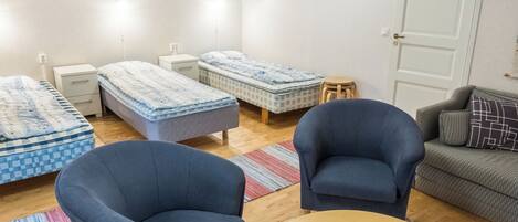 Een kamer met drie eenpersoonsbedden, een slaapbank, twee fauteuils en een kleine tafel.
