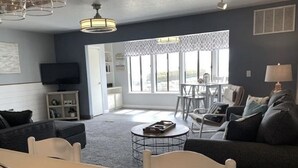Una sala de estar moderna con comedor, ventanas amplias y un televisor en la pared.