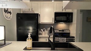 Una cocina con un refrigerador negro, un microondas y un horno. Hay una botella de jabón de manos en la encimera.