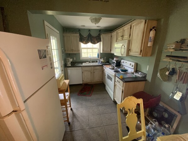 A compact kitchen with basic appliances, a window with curtains, and a tiled floor. - Longrifle Lodge (Westminster)