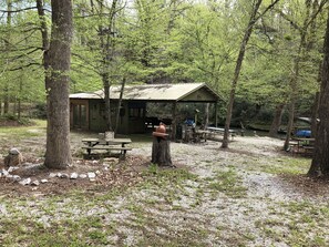 A rustic cabin with a picnic table and a covered area, surrounded by trees and a gravel path. - Longrifle Lodge (Westminster)