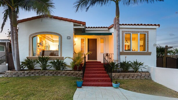 A two-story house with a red carpeted staircase leading to the front door, surrounded by palm trees and potted plants. - La Playa | Charming Bayside Bungalow (San Diego)