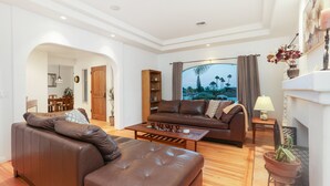 A spacious living room with a brown leather sofa, a wooden coffee table, and a large window with a view of palm trees. - La Playa | Charming Bayside Bungalow (San Diego)