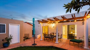A patio area with a pergola, outdoor seating, and a door leading to a room. - La Playa | Charming Bayside Bungalow (San Diego)