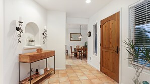 A hallway with a wooden door, a dining area with chairs and a table, and a potted plant. - La Playa | Charming Bayside Bungalow (San Diego)