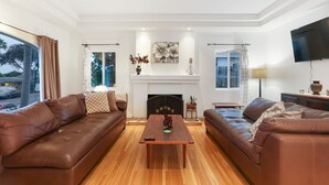 A spacious living room with two leather sofas, a wooden coffee table, and a fireplace. - La Playa | Charming Bayside Bungalow (San Diego)