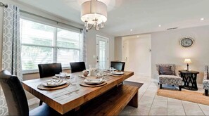 Un coin repas avec une table en bois dressée pour quatre personnes, un lustre et une horloge au mur.