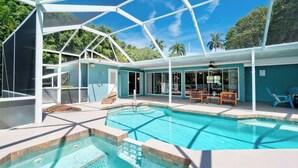 Ein Poolbereich mit Glasveranda, Liegestühlen und Blick auf die umliegende Bepflanzung.