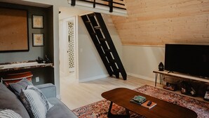 Un salon de style industriel, avec un plafond haut, un escalier, un canapé, une table basse et un téléviseur.