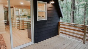 Une terrasse en bois avec un banc, une porte vitrée donnant sur un espace intérieur et une fenêtre donnant sur une forêt.