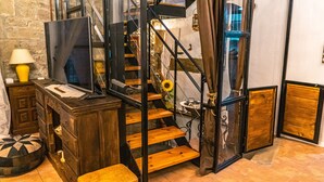 A staircase with wooden steps and metal railings, a desk with a lamp, and a small round ottoman.