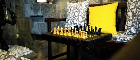 A chessboard set on a table in a room with stone walls, patterned cushions, and a statue.