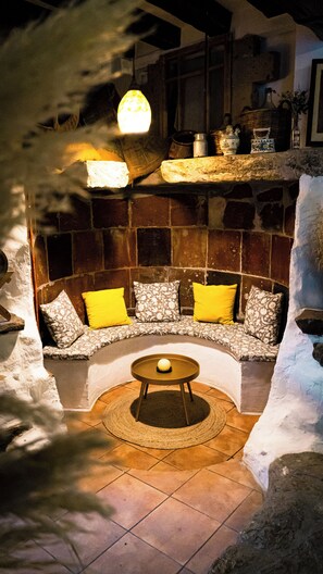 A cozy seating area with a sofa and cushions, a round table with a single chair, and a hanging light fixture. - Casa Rural (Hostafrancs)