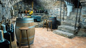 A rustic cellar with stone walls, wooden barrels, and a variety of bottles.