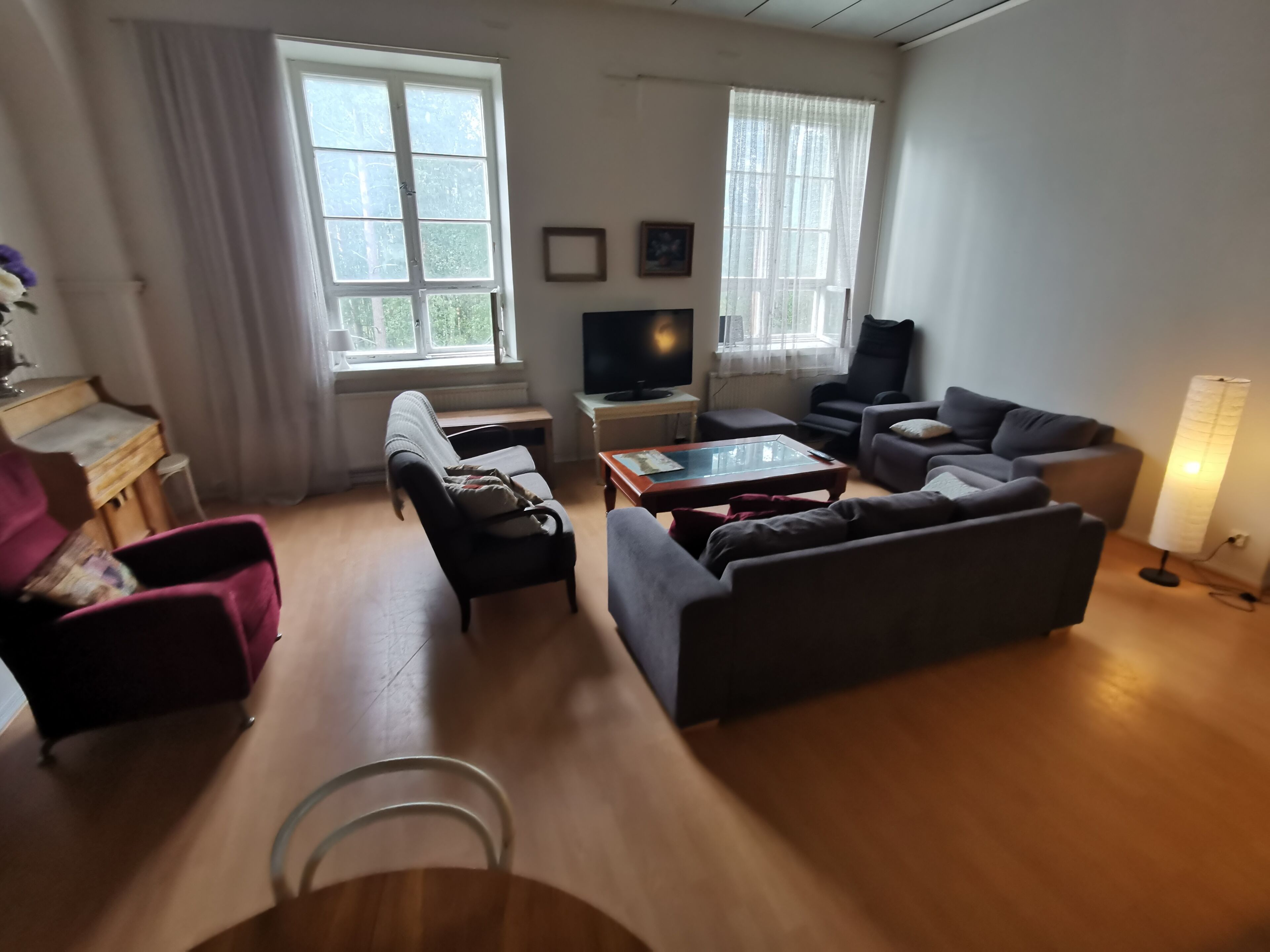 Una sala de estar con sofá, sillón y mesa de centro. Hay un televisor y una lámpara sobre una mesita.