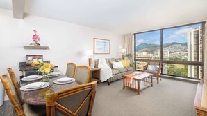 A modern living room with a dining area, large windows with a city view, and a cozy seating arrangement.