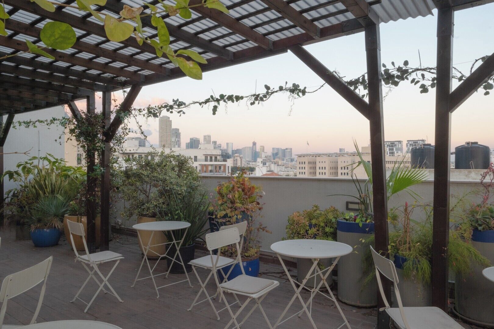 A rooftop terrace with potted plants, foldable chairs, and a view of the city skyline.
