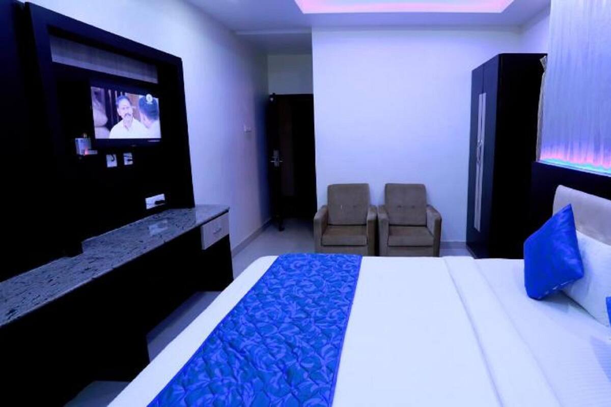 A hotel room with a bed, two armchairs, a TV, and a minibar.