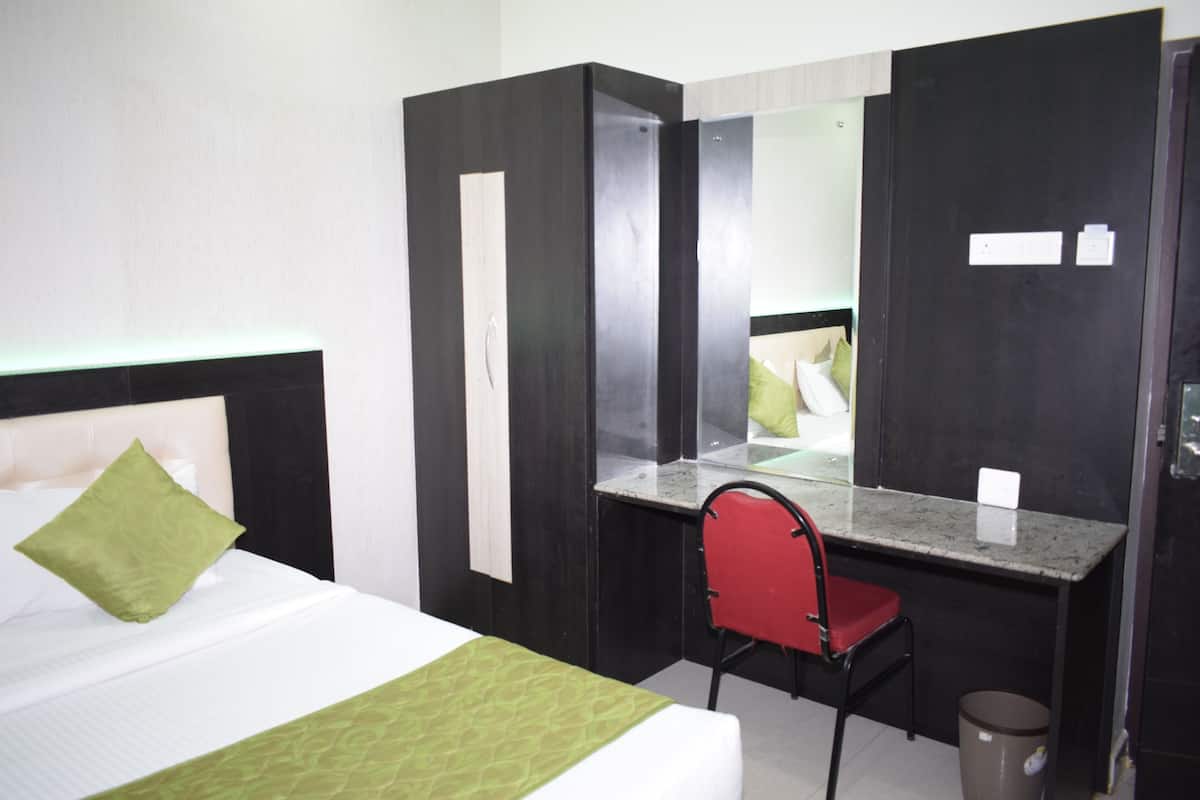 A hotel room with a bed, a desk with a chair, a mirror, and a trash bin.