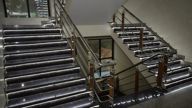 Un conjunto de escaleras metálicas iluminadas con barandilla de vidrio, que conducen a un piso superior.