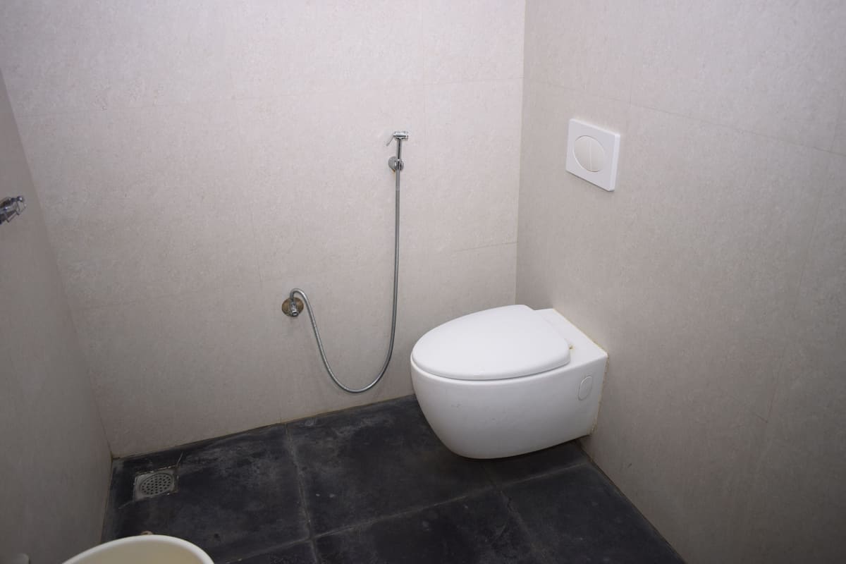 A small, compact bathroom with a white toilet, a showerhead, and a floor drain.