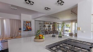 A modern kitchen with a central island, gas stove, and a dining area with chairs and a table. - Spacious beach front Vila with 100 sqm infinity pool,  a basket ball court (Rhodes)