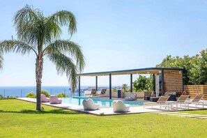 A modern outdoor pool area with lounge chairs and a covered seating area, overlooking a clear blue sky and a distant view of the sea. - Spacious beach front Vila with 100 sqm infinity pool,  a basket ball court (Rhodes)