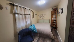 Ein kleines Schlafzimmer mit einem Bett, einem Sessel, einem Regal mit Gegenständen und einer Wand mit einer Astdekoration.