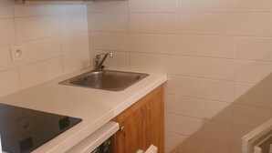 A kitchen with wooden cabinets, a stainless steel sink, and white tiled walls. - Charming 32m² studio, balcony, near slopes, Les Menuires (Les Menuires)