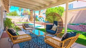A covered patio with wicker furniture, a hanging chair, and a pool. - Cozy 3BR Home with Pool & Spa - 9 Mi to LV Strip! (Henderson)