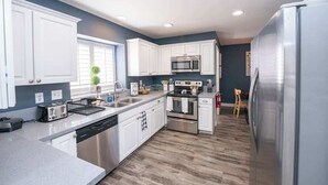 A modern kitchen with white cabinets, stainless steel appliances, and a wooden floor. - Cozy 3BR Home with Pool & Spa - 9 Mi to LV Strip! (Henderson)