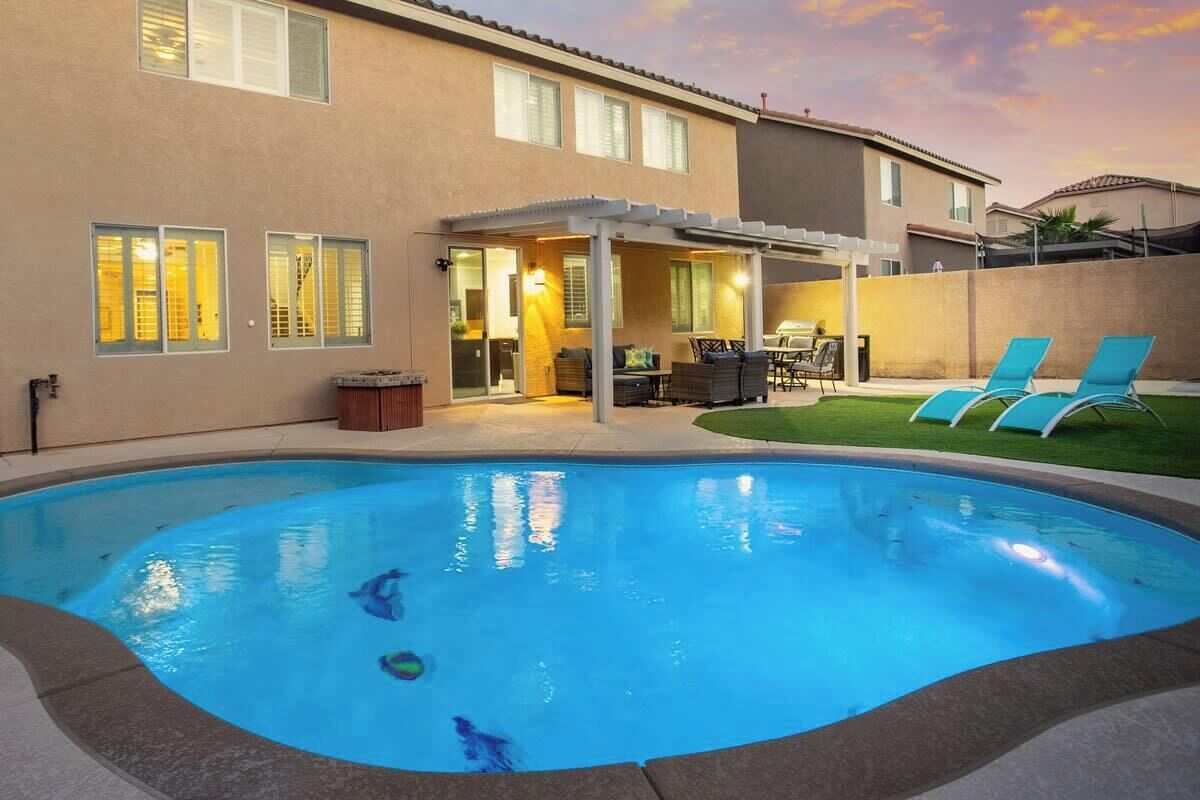 A swimming pool with a covered patio area, a lawn, and a house in the background.