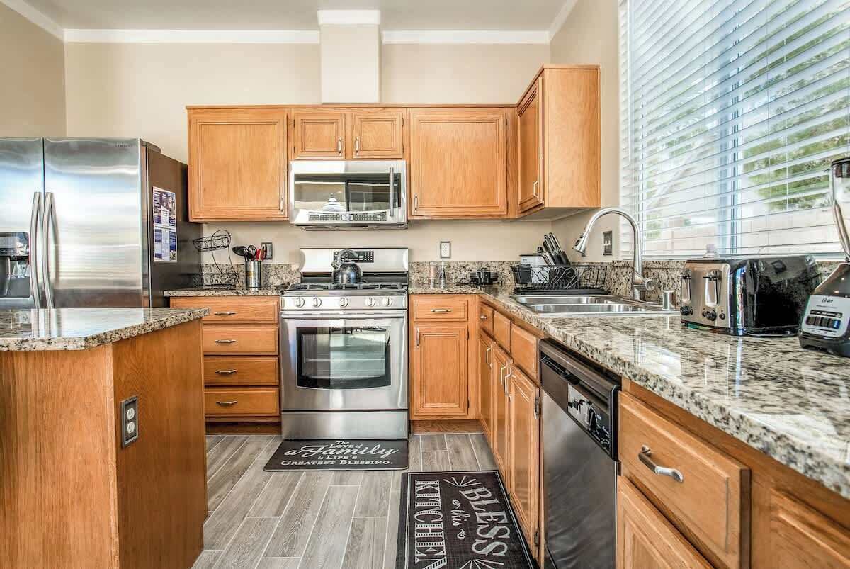 A modern kitchen with wooden cabinets, stainless steel appliances, granite countertops, and a built-in oven.