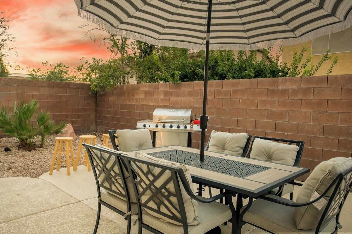An outdoor patio with a grill, a table with chairs, and an umbrella.