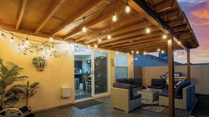 An outdoor patio area with wicker furniture, string lights, and a view into the house.