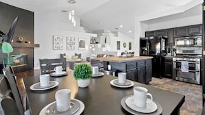 A modern kitchen with dark cabinetry, stainless steel appliances, and a dining area with a dark wooden table set for four.