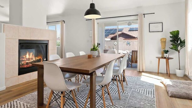 A modern dining area with a fireplace, a wooden table, white chairs, and a large window overlooking a garden. - Royal Skyline -Spacious & Modern 3BR w Pool (Henderson)