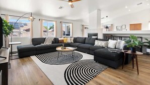 A modern living room with a sectional sofa, a round coffee table, and a black and white patterned rug. - Royal Skyline -Spacious & Modern 3BR w Pool (Henderson)