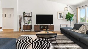 A modern living room with a flat-screen TV, a dark sofa, a coffee table, and a striped rug. - Royal Skyline -Spacious & Modern 3BR w Pool (Henderson)