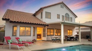 A two-story house with a swimming pool, a patio with outdoor furniture, and a covered area with a table and chairs.