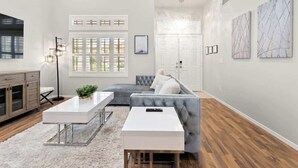A modern living room with a grey sofa, white coffee table, and a large window with blinds.