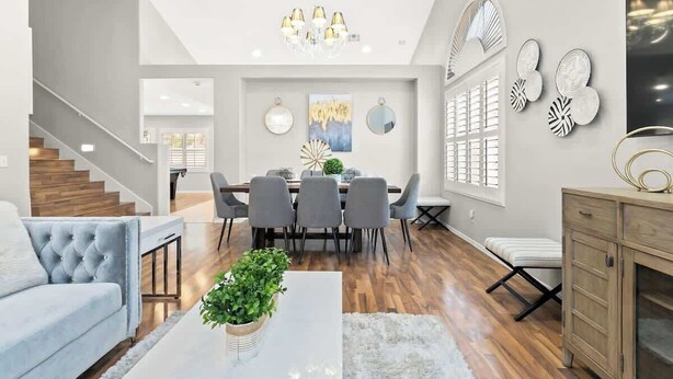 A modern living room with a grey sofa, a coffee table with a plant, a dining area with a chandelier, and a staircase.
