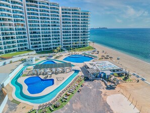 Ein Resort mit mehreren Schwimmbecken, einem Strandbereich und einem großen Hotelgebäude.