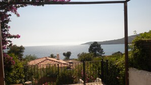 A patio with a stone floor, a table with a floral tablecloth, and a view of the sea.