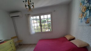 A bedroom with a bed, a dresser, a window, and an air conditioning unit.
