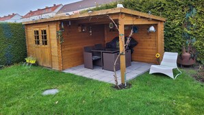 A wooden outdoor structure with a table and chairs, surrounded by a well-maintained lawn and a hedge. - Vacation apartment RuBi - Holiday apartment (Stralsund)