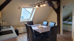 A dining area with a table and chairs, a window with a view, a kitchen with a sink and stove, and a bedroom with a bed. - Vacation apartment RuBi - Holiday apartment (Stralsund)