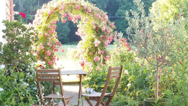 A garden with a wooden table and chairs, surrounded by a variety of plants and flowers. - stylish, idyllic apartment with mountain view (Stegen)